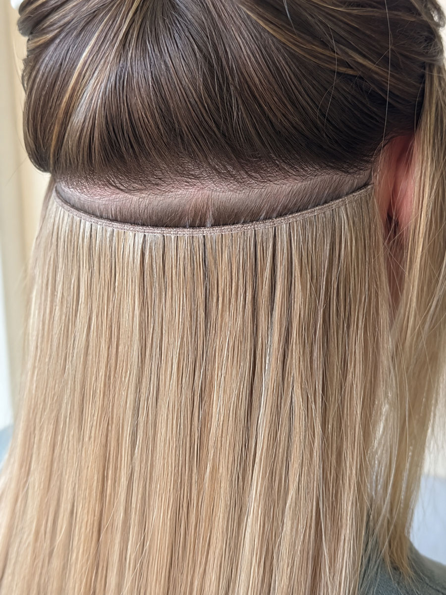 A machine weft row being fitted flat against the scalp, showing the fine top edge of the weft