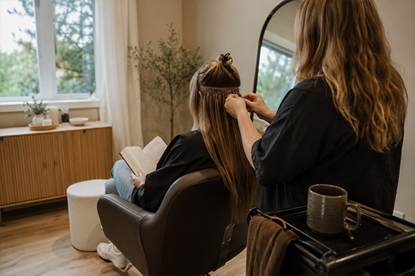 A client seated with her hair sectioned and clipped while a weft row is fitted behind her